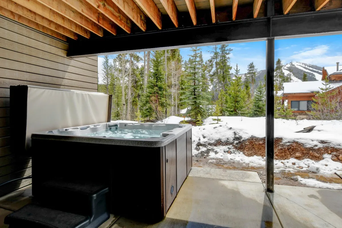 A steamy outdoor hot tub sits on a deck overlooking a snowy forest and distant mountain peaks. The inviting, tranquil setting suggests relaxation and rejuvenation after a day filled with outdoor excitement.