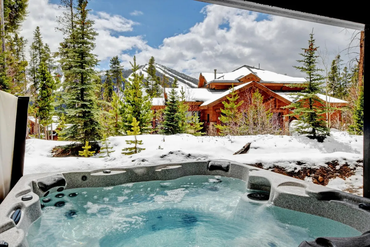 This image features a luxurious hot tub set on a private deck, surrounded by snow-covered trees and with majestic mountains in the background. The wooden cabin and the serene atmosphere evoke relaxation and exclusivity, perfectly suited for unwinding after mountain adventures.