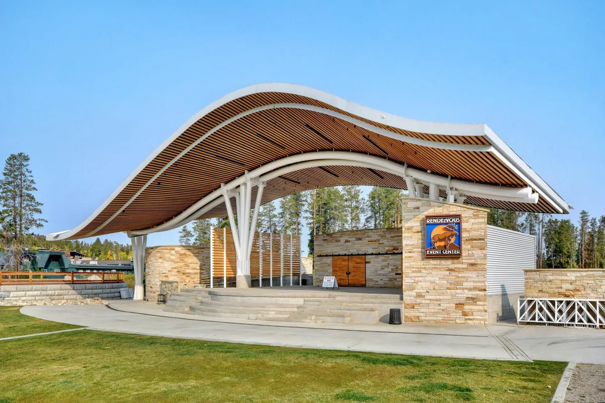 An exterior shot of a curved-roof event space with sturdy stone walls and an open stage area. The scene hints at lively outdoor performances, local festivals, and cultural celebrations under the stars.