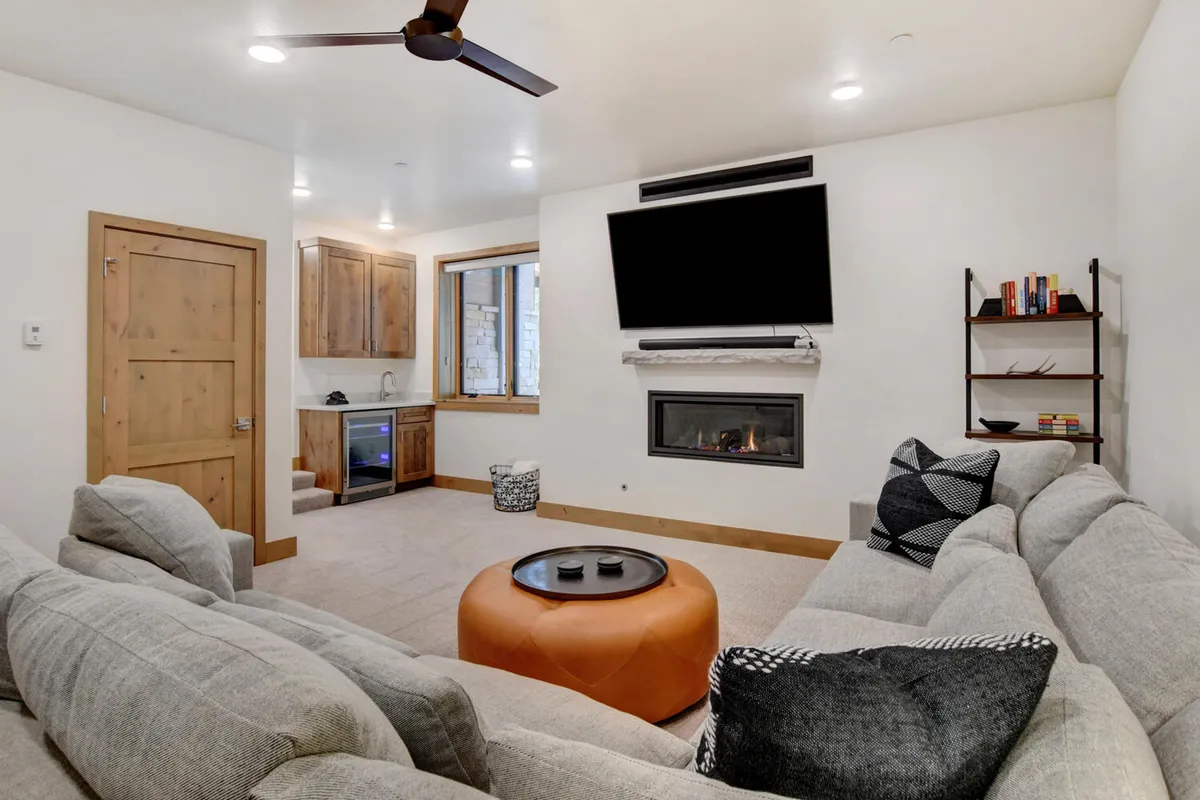 A spacious entertainment lounge featuring a plush sectional sofa, a cozy fireplace, a coffee table, and a large bookshelf filled with books and games. The setup is perfect for movie nights, reading, or gathering with friends and family.